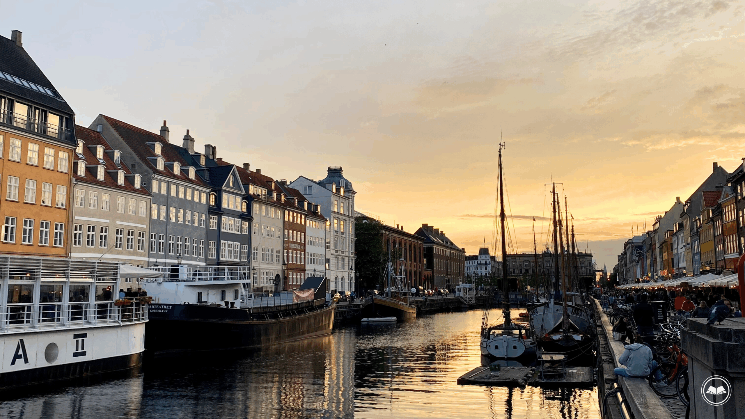 sunset reflecting on the water in copenhagen, denmark with boats and colorful buildings around